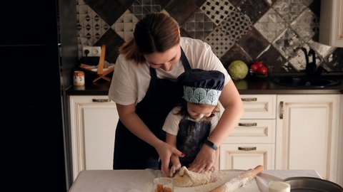 Close-up of mother and little daughter kneading dough together in the kitchen. Mother teaches daughter to prepare dough for cookies.