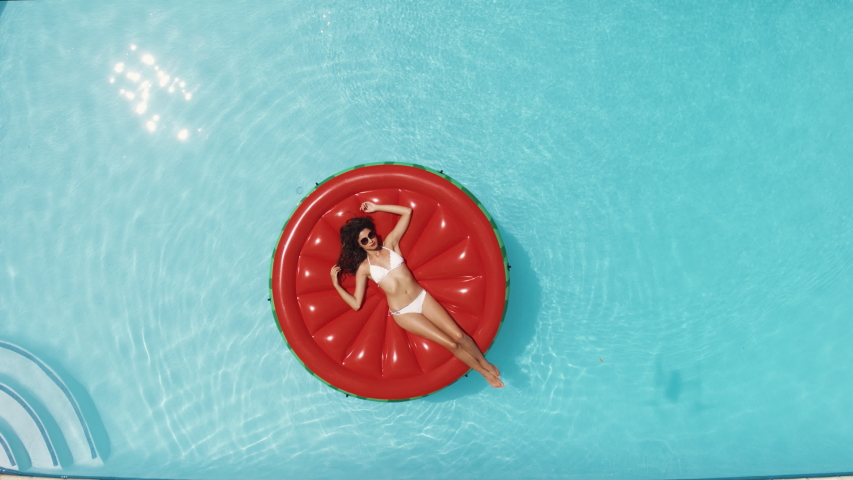 Aerial view of a young woman lying on an inflatable red mattress floating and relaxing in the swimming pool. Female relaxing on a raft in the pool on a sunny day.
 | Shutterstock HD Video #1046860672
