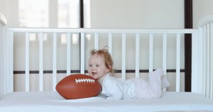 Caucasian baby playing with American football ball in bed. RAW Graded footage 4K slow motion 50fps