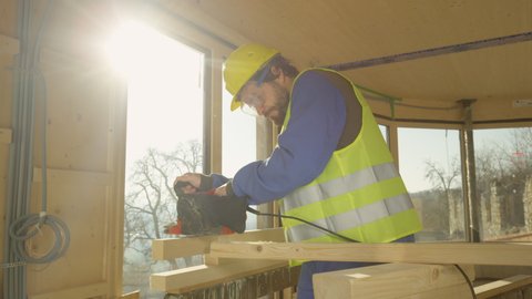 SLOW MOTION, CLOSE UP, LENS FLARE: Small wooden beam falls on the ground as contractor tries to sand it. Clumsy builder using an electric sander to buff a plank drops the piece wood on the ground.