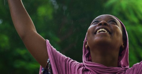 Authentic shot of young happy carefree beautiful african woman wearing burqa is feeling free under the rain on a background of a village. Concept: freedom, happiness, life, love for nature