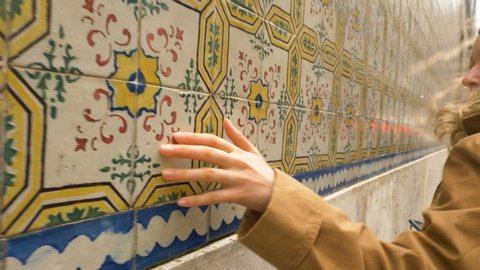 girl tourist walks along old Lisbon street touching with hand azulejo tiles pictures on historical building walls close view