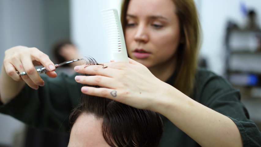 Stylish man sitting barber shop Hairstylist Hairdresser Woman cutting his hair Portrait handsome happy young bearded caucasian guy getting trendy haircut Attractive barber girl working serving client 