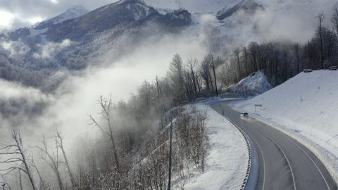 Drone view suv car driving on winding road in winter mountains. Winter serpentine road on snowy mountain peak and forests aerial landscape. Cloudy mountain landscape from above. Near past the lantern