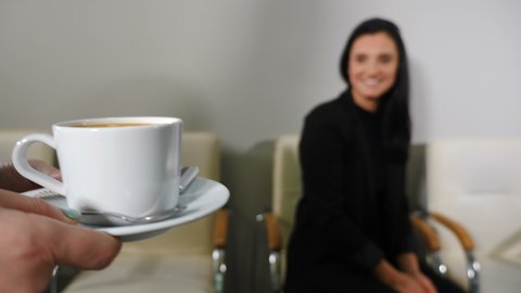 Office life concept. Female hands of receptionist or secretary bringing coffee to pretty female client in office. Steadicam shot. secretary carring a cup of coffee. Close-up. Focus on cup. 4k footage