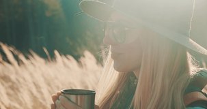 Close-up Woman hiking backpacker traveler drinking hot tea and relaxing in the fall forest on sunny autumn day. Beautiful mountain landscape view. 4K slow motion video.
