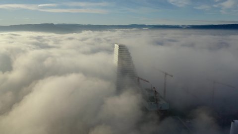 Basel, Basel-Stadt / Switzerland - January 08 2020 09:00AM: Waves of sea of fog over the Basel city colliding with the Roche tower at sunrise. Fly around shot from a drone.
