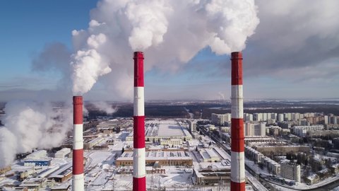 Industrial zone with a large red and white pipe thick white smoke is poured from the factory pipe in the beautiful winter sunny day. Pollution of the environment: a pipe with smoke. Aerial view, 4K.
