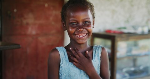 Authentic portrait of happy rural african girl is smiling in camera on a village background. Concept: charity, poverty,life, happiness, authenticity, religion