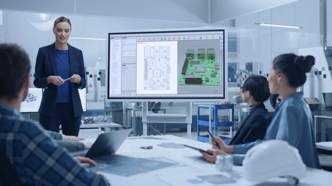 Modern Industrial Factory Meeting: Confident Female Computer Engineer Uses Digital Interactive Whiteboard, Talks to a Group of Engineers, Managers Talks and Shows 3D Printed Circuit Board Concept