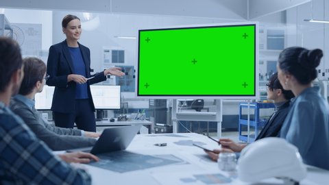 Modern Industrial Factory Meeting: Confident Female Engineer Uses Interactive Green Mock-up Screen Whiteboard, Makes Report to a Group of Engineers, Managers