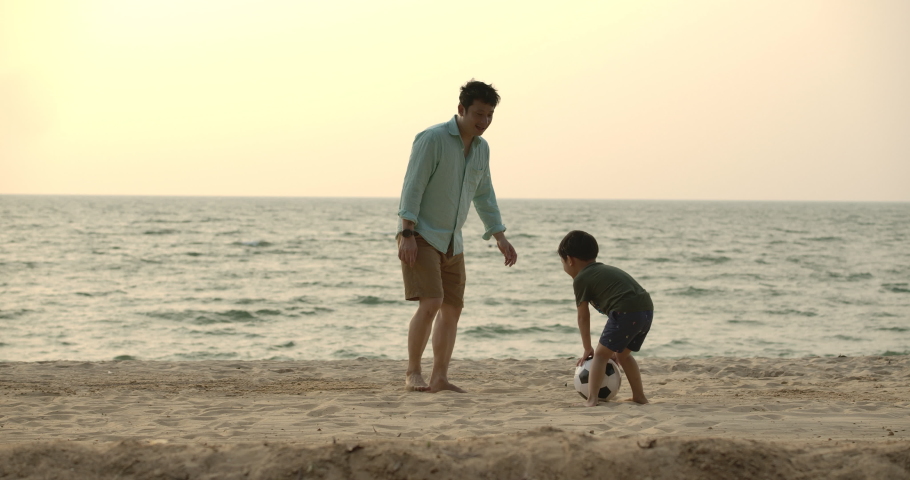 Asian Father and son playing together with ball in football on the beach under sunset background. Slow motion. Happy family concept.  Royalty-Free Stock Footage #1046910916