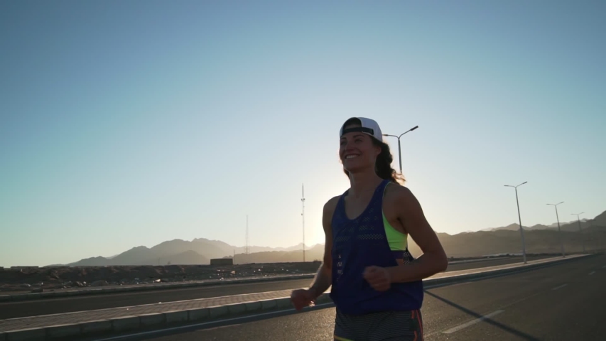 Smiling caucasian girl jogging at highway in mountains rapid slow motion