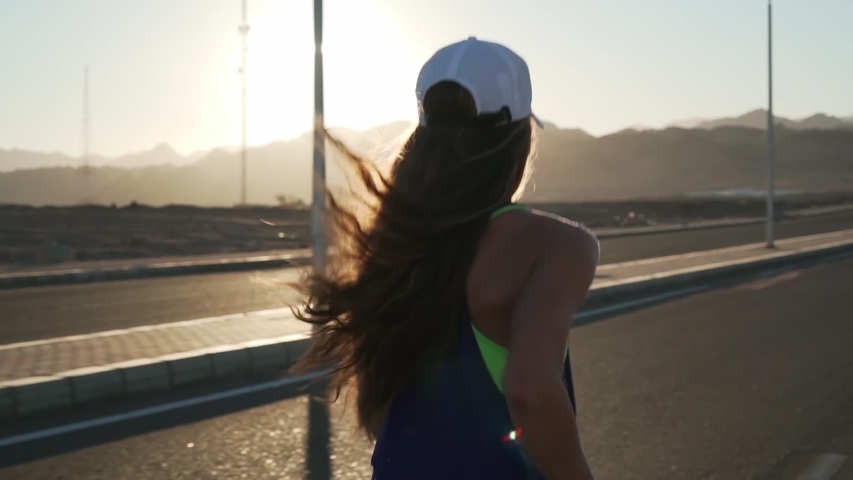 Rear view of young slim girl jogging at highway in mountains rapid slow motion