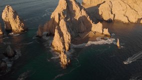 4K drone shot that pulls back to reveal the famous tourist Arch near Cabo San Lucas where the beautiful sea sends waves crashing against jagged cliffs at sunrise