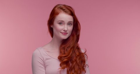 Natural Beauty red-haired Girl touching her perfect wavy Hair and smiling. Portrait of Amazing young Girl looking cute to the Camera, wearing pink Top, nude Makeup. Healthy Skin and Hair. Care. Girl.