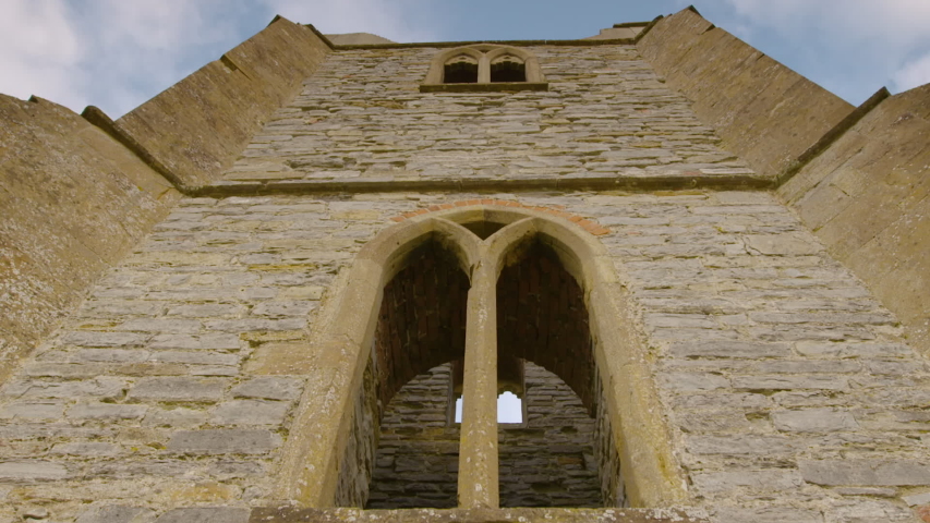 Close-up low angle daytime front view tilting shot of a historical stone-wall ancient church building ruin with arch windows and door against sky background, Aberdeenshire, Scotland, UK