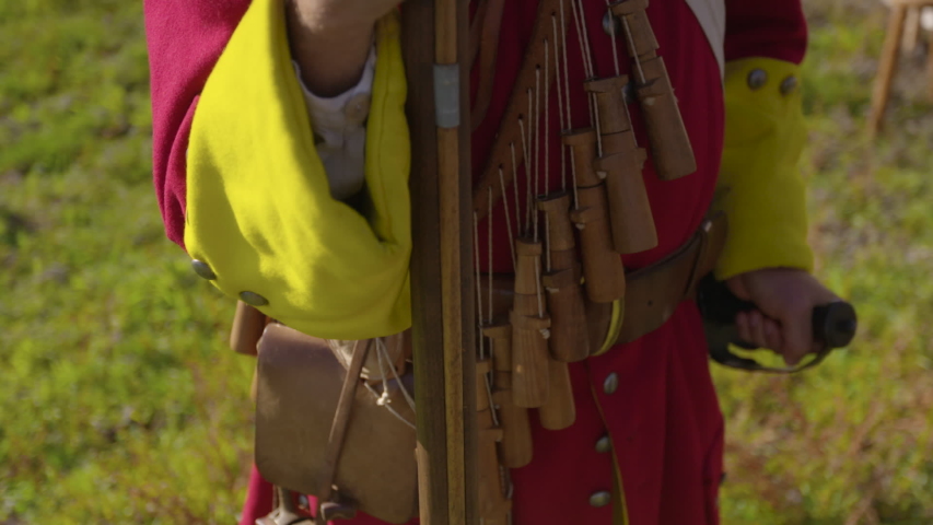 A daylight closeup shot of a man wearing a red and yellow vintage uniform of a soldier while holding the barrel of a wooden shotgun.