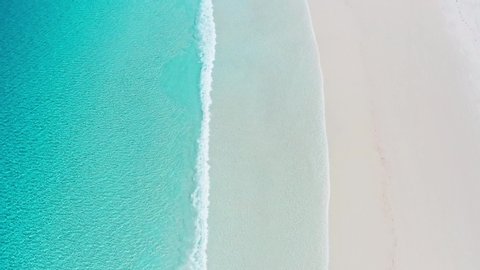 Aerial shot of turquoise water and waves rolling in from left to right onto the sand of Australia's whitest beach - Lucky Bay