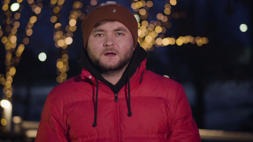Portrait of young Caucasian man in winter clothes getting snowball in face. Surprised positive guy smiling and looking at camera. Winter joy, leisure games, childish lifestyle, snowball fight.