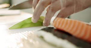 Restaurant kitchen. Male sushi chef prepares Japanese sushi rolls of rice, salmon, avocado and nori. prepares avocados