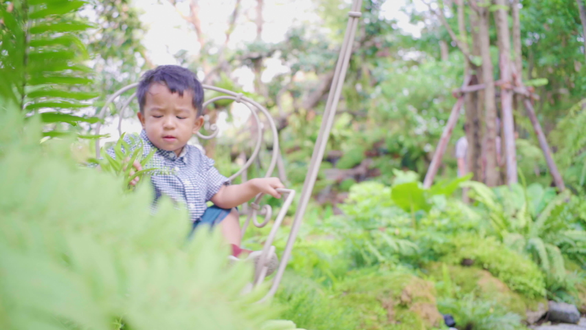 Smiling adorablae baby asian boy enjoying on swing playground in green tree park
