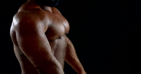 naked strong man is showing his muscles, tensing body, turning in front of camera in studio