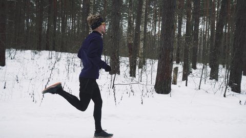 Running Man In Sportswear Workout Before Triathlon. Runner Man Running Winter Forest Snow Trail. Winter Sports And Recreation Concept. Young Man Training Jogging Outdoor In Winter. 