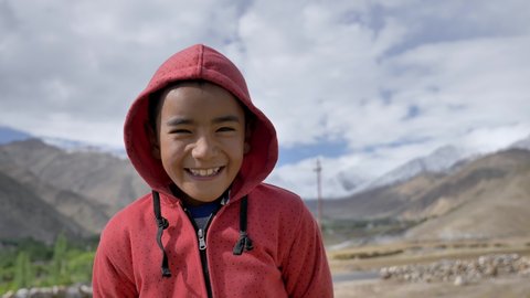 A smiling Asian kid wearing hoodie and standing outdoors in mountainous region in upper Himalayas. A happy and cute young nomad boy looking at a camera with a smile on his face.