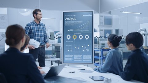 On a Meeting Chief Industrial Engineer Reports to a Group of Specialists, Managers, Uses Digital Whiteboard to Show Statistics with Graphs, Company Productivity Growth. Successful Industrial Factory