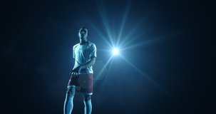 4K slow motion video of a male soccer player makes a dramatic play. The background is dark behind him. Only one of the lights shine brightly. Animation of splashes and flames added.