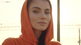 A close-up view of a calm young woman is in a hood is looking to the camera and to the side outdoors in the morning