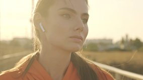 A calm focused woman is standing with earphones in her ears while training outdoors on a sunny morning