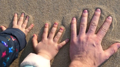 Adult and Children Hands Leave Handprint on Sandy Beach at Sunset