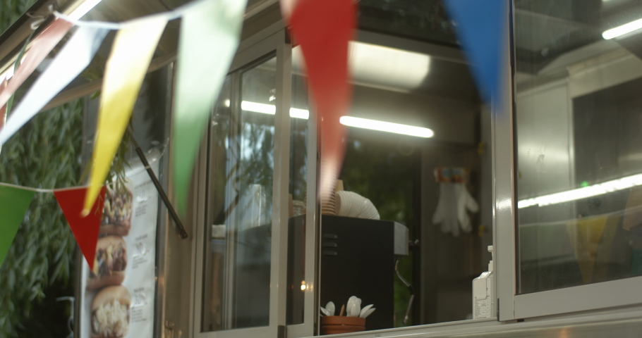 African American joyful young man barman looking out window of festive food truck with two hot dogs in hands. Male waiter smiling while giving order. Handsome cheerful vendor of small cafe. Royalty-Free Stock Footage #1046965987