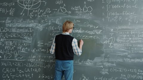 Maths teacher is writing formulas on chalkboard then talking teaching class at school during mathematics lesson. Education, occupation and people concept.