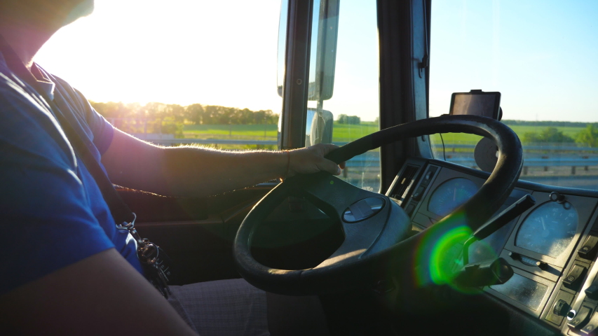 Unrecognizable man sitting behind wheel of his truck and riding through countryside at sunset. Close up steering wheel and dashboard of truck. Beautiful landscape at background. Slow motion Side view Royalty-Free Stock Footage #1046970022