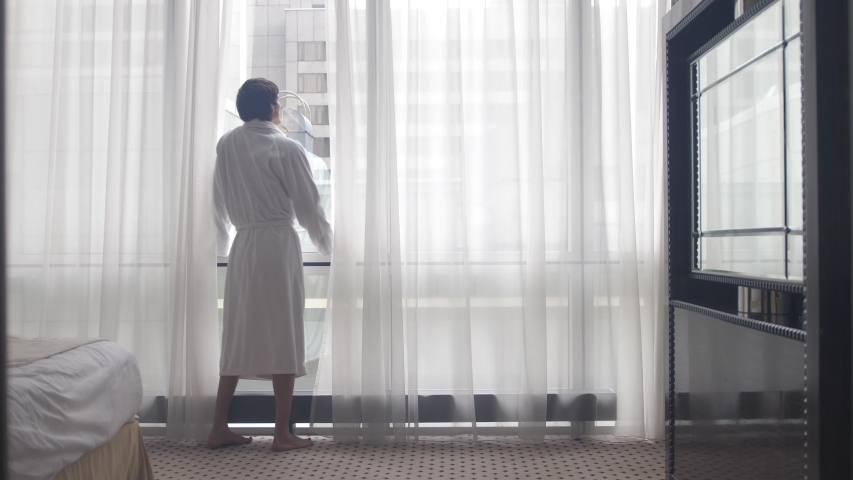 Young man wearing bathrobe drinking coffee by the window | Shutterstock HD Video #1046970241