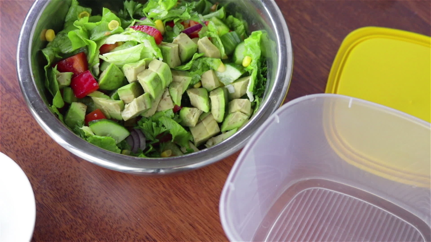 put fresh salad with  cucumber  tomaotes avocado corn  lettuce parsley in to plastic food container with serving tongs
