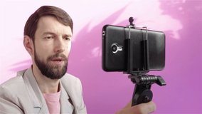 handsome bearded man blogger recording video on smartphone live streaming on pink background
