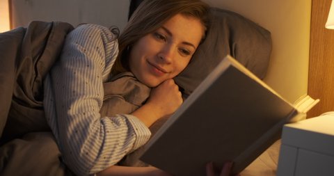 Woman reading a book in bed at night
