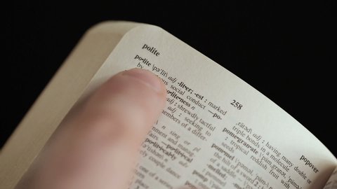 close up shot of Man looking for word by finger in English explanatory Dictionary on black background