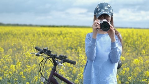 Amateur photographer. A young photographer girl in a cap make photos of rape field.
