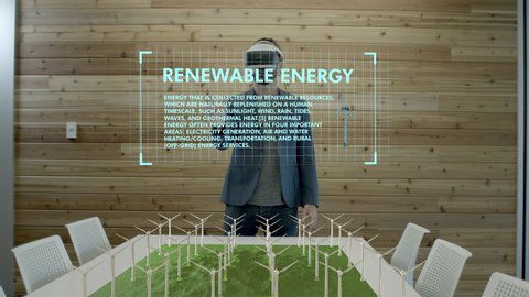 Hip businessman wearing VR Virtual Reality glasses looks into the future of Green Energy Windmill technology. Stats and data flow by. 