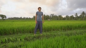 A young man has a yoga training on a beautiful rice field. Travel to Asia concept. Slowmotion video
