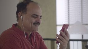 A happy old man using smartphone and earphones to chat with a wife over a video call in a long distance relationship. Smiling Grandpa talking with his son friend working abroad in indoor home setup.  - Powered by Shutterstock - Get 15% off with code: PIKWIZARD15