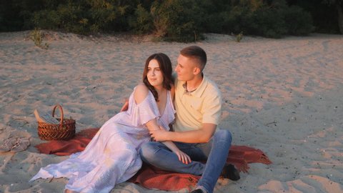 Loving couple sits on a sandy beach, on the shore of a lake, river. Sunsets sunset in summer, sunlight.Romantic couple during the sunset. Nature.