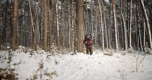 Mature male hiker in warm winter clothing carrying on big backpack while walking among snow-covered woods. Bearded man spending leisure time on frosty seasonal nature.