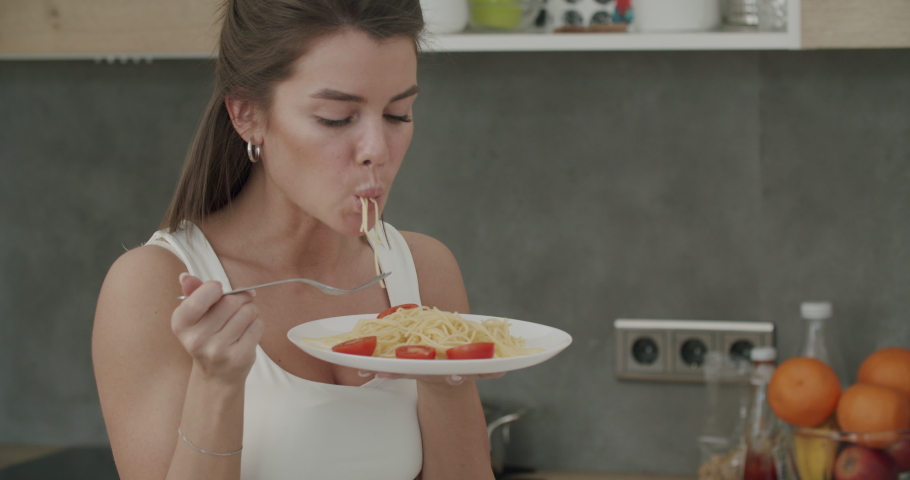 Italian food. Close-up of healthy caucasian woman eating spaghetti with tomatos. Perry girl in home clothes having fun with vegeterian pasta. 4k raw footage slow motion