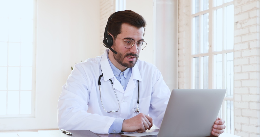 Professional male doctor in white medical coat and headset making conference call on laptop computer, consulting distance patient online in video chat, explain treatment by webcam concept Royalty-Free Stock Footage #1047021451
